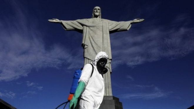 A worker wearing protective clothing stands in front of the Christ the Redeemer statue in Brazil